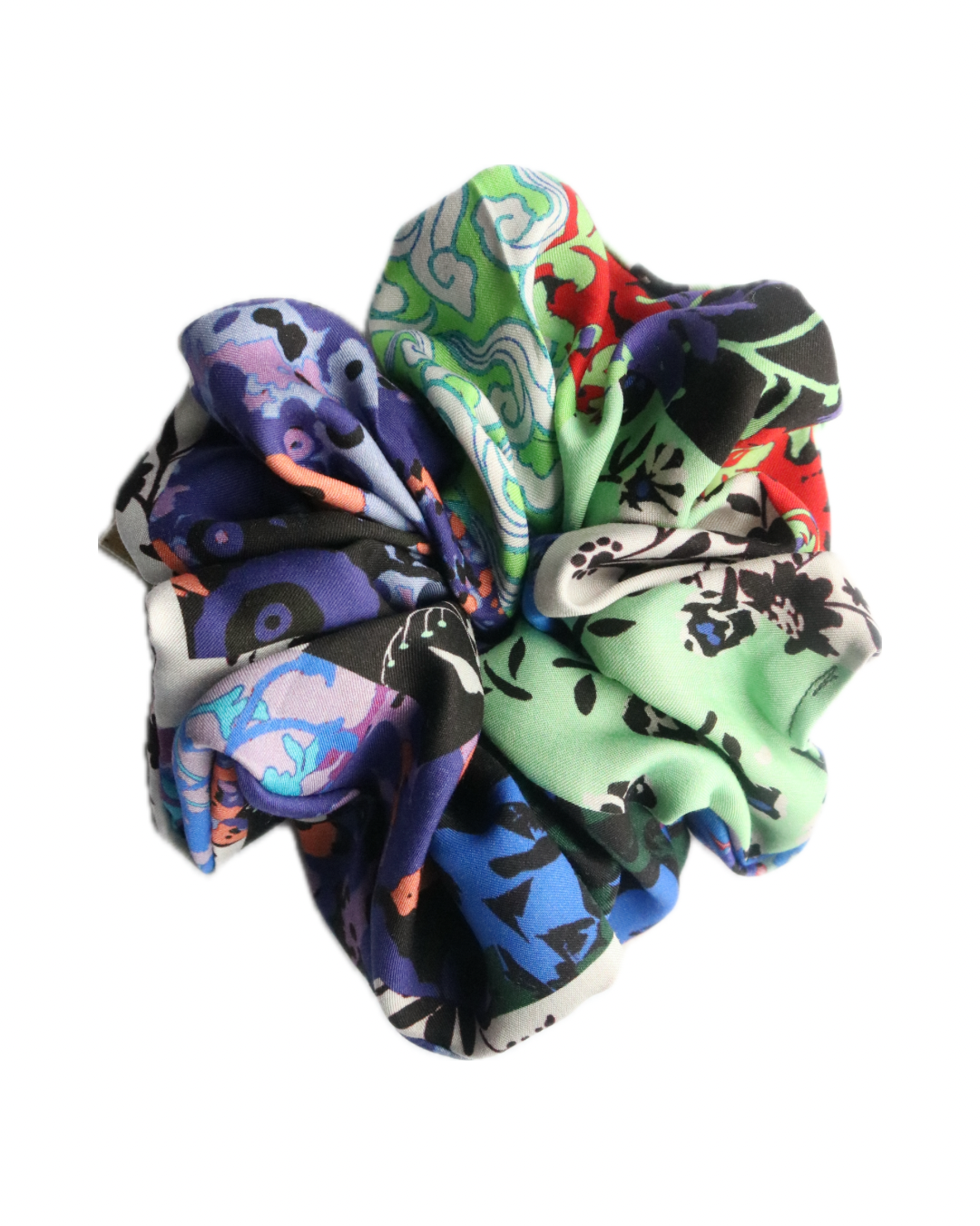 A vibrant scrunchie made from deadstock fabric, featuring a multicolored pattern with shades of green, blue, red, black, and white. The fabric is gathered and ruffled, creating a voluminous, textured appearance. The design includes abstract and floral elements, giving it a unique and artistic look. The scrunchie is photographed against a white background.